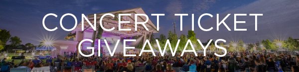 A wide-angle photo of a packed outdoor concert venue at sunset, with a large crowd gathered in front of a covered stage. Bold white text across the center reads “CONCERT TICKET GIVEAWAYS.” The sky has a soft pink and purple gradient, adding to the festive atmosphere.
